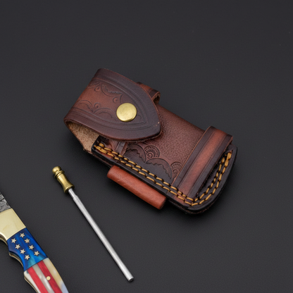 Close-up of the embossed leather sheath, sharpening rod loop, and mini sharpening steel on a black-charcoal background