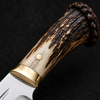 Extreme close-up of natural dark stag horn Bowie knife handle with gold brass bolster on deep black charcoal background