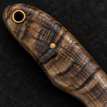 Extreme close-up of natural ram horn Damascus skinner knife handle with brass pin and lanyard hole on deep black charcoal background