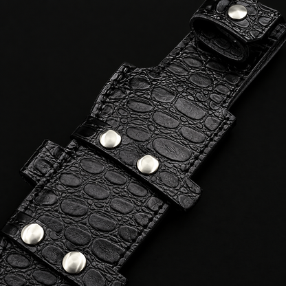 Extreme close-up of black crocodile embossed genuine leather horizontal carry sheath with silver rivets on pure black background