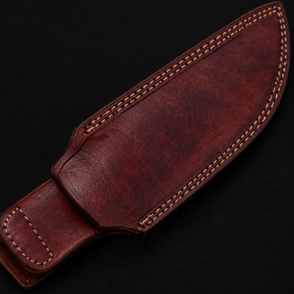 Extreme close-up of deep burgundy genuine leather machete knife sheath diagonal angle tan stitching on pure black background