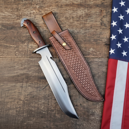 Hand forged high carbon Bowie hunting knife with rosewood sub hilt and brown basketweave leather sheath on dark rustic wood with a USA flag