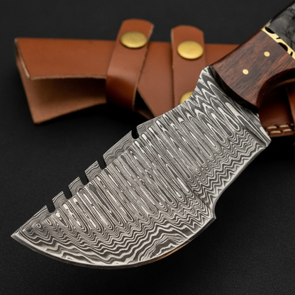 Extreme close-up of wide Damascus tracker blade with fuller grooves and layered pattern on black charcoal background