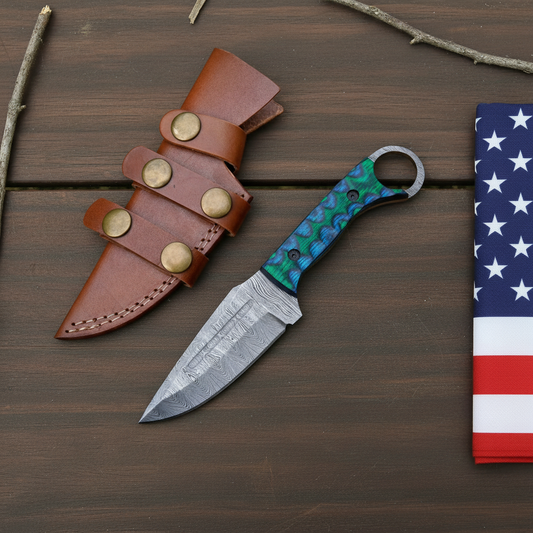 Damascus ring knife and leather sheath on dark brown wood beside a USA flag
