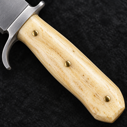 Extreme close-up of pale natural camel bone handle with brass pins and steel finger guard on deep black charcoal background