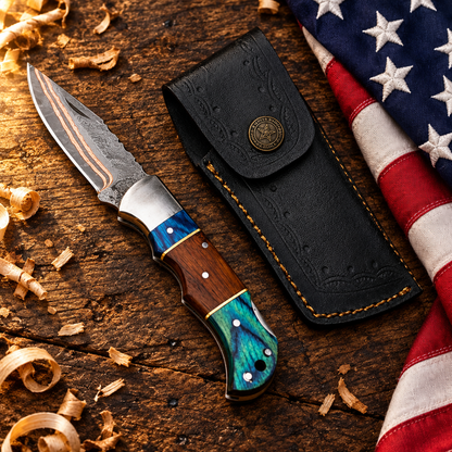 Handmade copper Damascus folding pocket knife open showing copper Damascus blade teal pakka wood rosewood handle hero flat lay on rustic dark wood with American USA flag