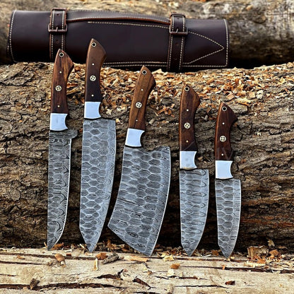 Handforged 5-piece Damascus steel kitchen chef knife set with walnut handles brass pins steel bolsters leaning against log with dark brown leather roll bag outdoor