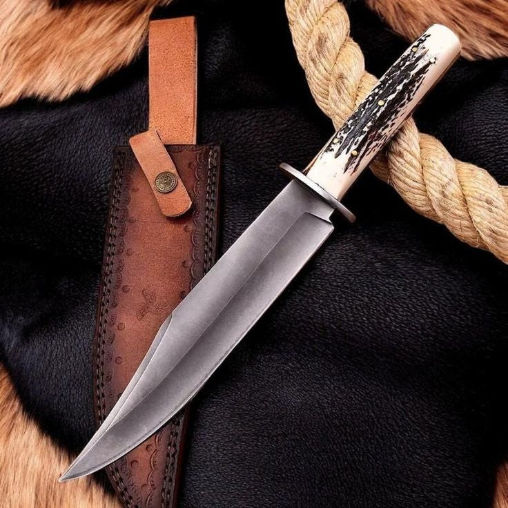 Custom handmade carbon steel hunting survival knife with pale stag antler handle steel crossguard and brown leather sheath on dark fur with rope